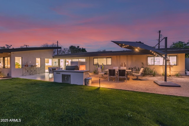 back of property at dusk with a lawn, a patio, an outdoor kitchen, and stucco siding