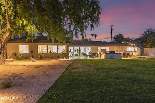 back of property at dusk featuring stucco siding, a yard, and a patio area