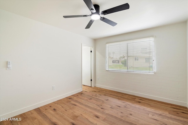 spare room featuring ceiling fan, light hardwood / wood-style flooring, and brick wall