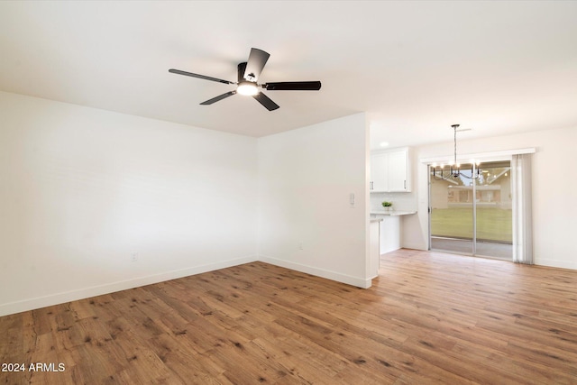 unfurnished room with ceiling fan with notable chandelier and light hardwood / wood-style floors