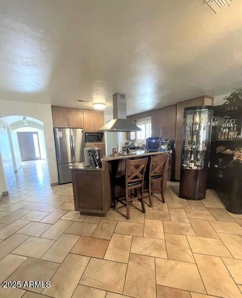 kitchen featuring appliances with stainless steel finishes, a breakfast bar area, island exhaust hood, kitchen peninsula, and a textured ceiling