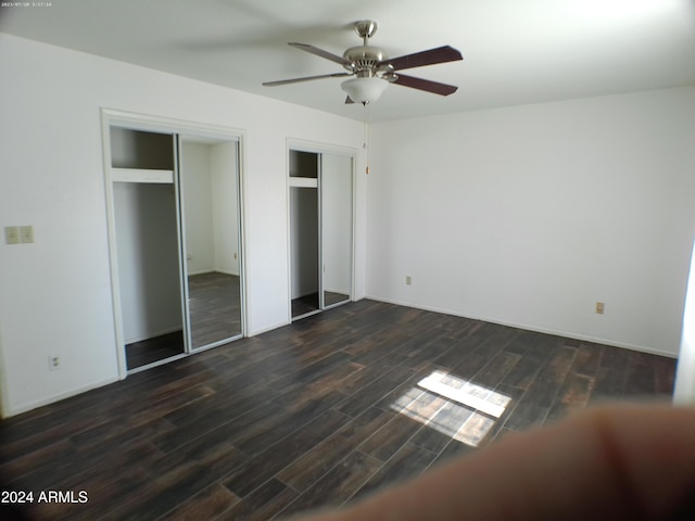 unfurnished bedroom with ceiling fan, dark wood-type flooring, and two closets