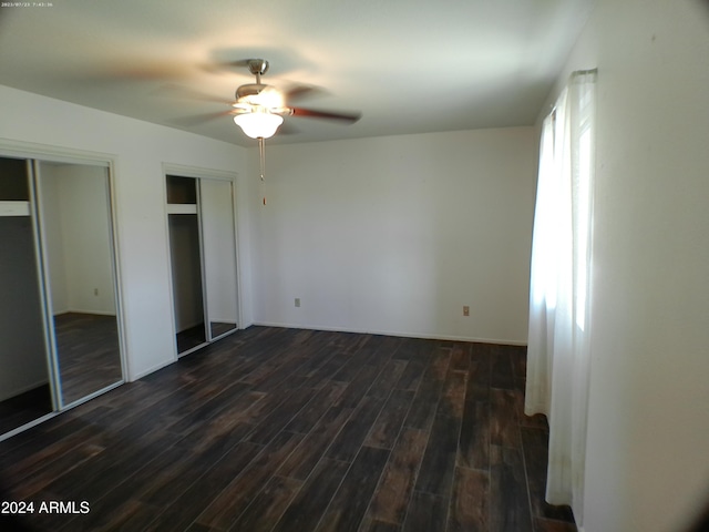 unfurnished bedroom with ceiling fan, dark wood-type flooring, and multiple closets