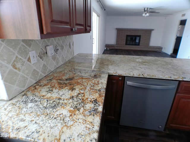 kitchen featuring tasteful backsplash, stainless steel dishwasher, light stone counters, ceiling fan, and a fireplace