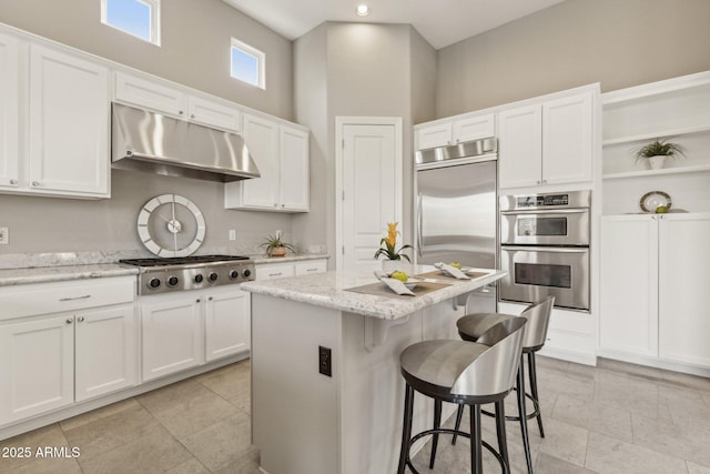 kitchen with light stone countertops, white cabinetry, appliances with stainless steel finishes, and a center island