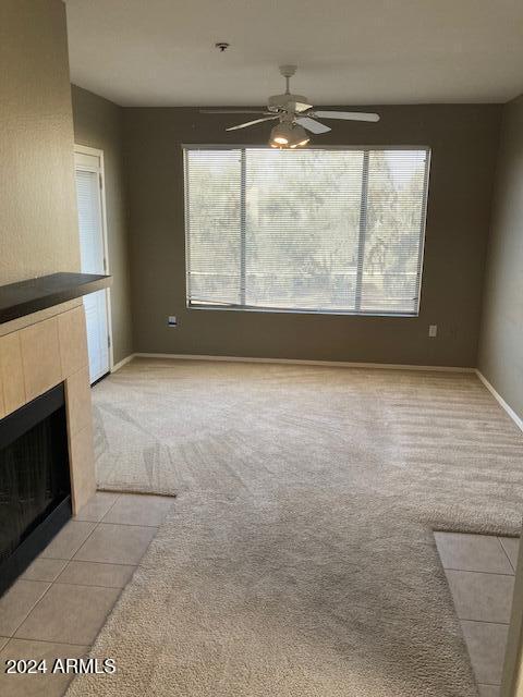 unfurnished living room with a tile fireplace, light colored carpet, plenty of natural light, and ceiling fan