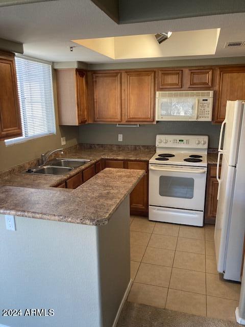 kitchen with kitchen peninsula, light tile patterned floors, white appliances, and sink