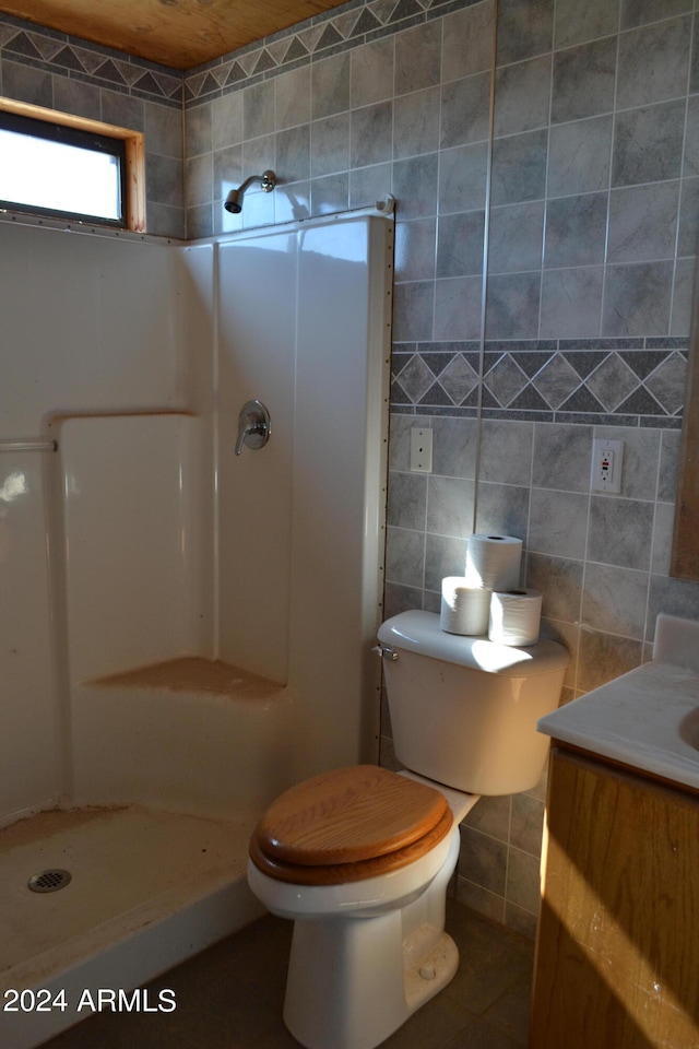 bathroom featuring toilet, vanity, tile walls, tile patterned floors, and walk in shower