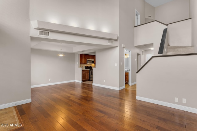 unfurnished living room featuring visible vents, baseboards, stairs, and dark wood-style floors