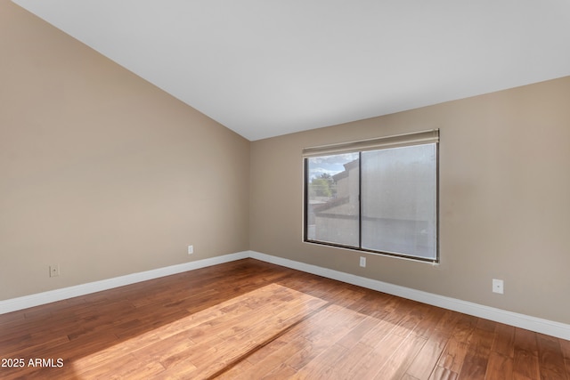 spare room with baseboards, wood finished floors, and vaulted ceiling