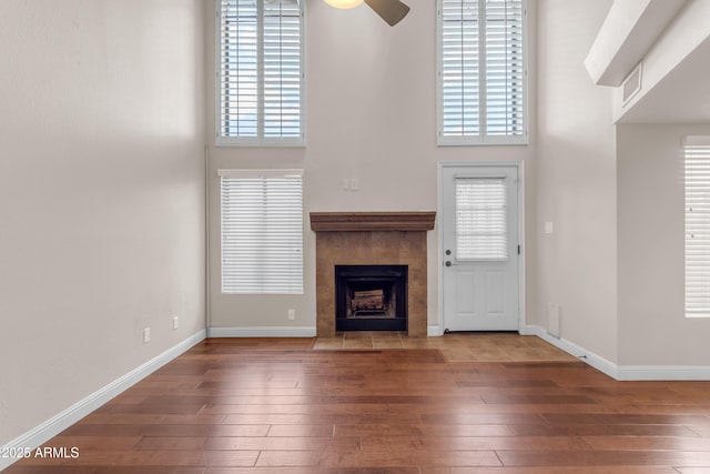 unfurnished living room with wood-type flooring, a ceiling fan, baseboards, and a tiled fireplace