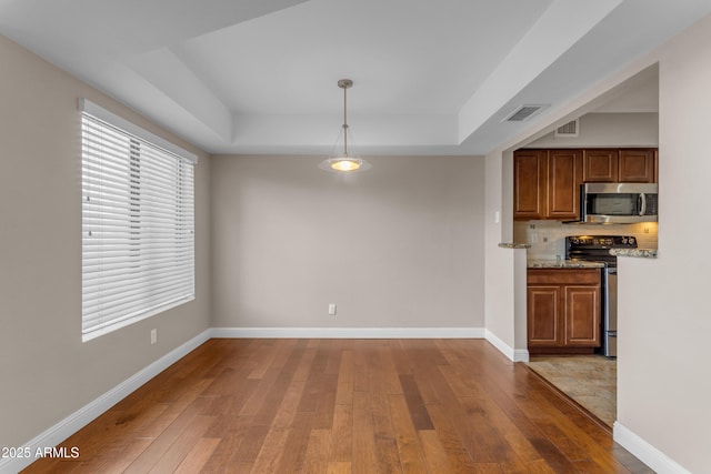 kitchen with brown cabinetry, visible vents, appliances with stainless steel finishes, light wood-type flooring, and a raised ceiling