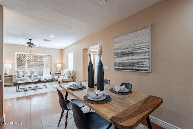 dining space featuring a textured wall, a ceiling fan, baseboards, visible vents, and light wood-style floors