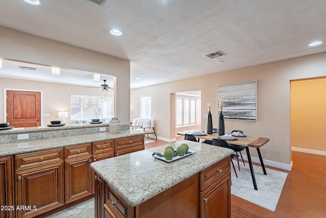 kitchen with light stone counters, a center island, brown cabinets, and light wood finished floors