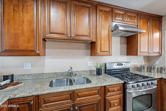 kitchen featuring light stone countertops, a sink, under cabinet range hood, and gas range