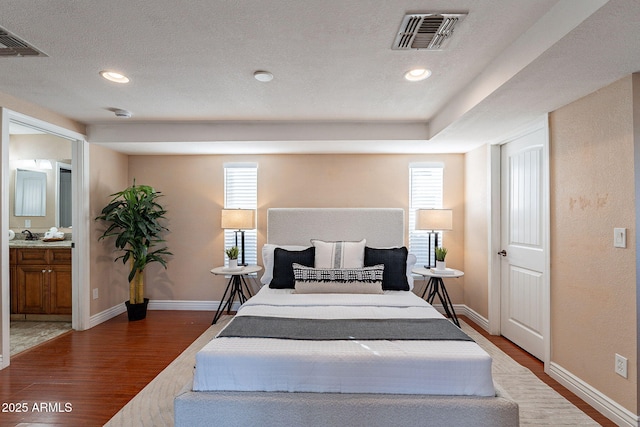 bedroom with connected bathroom, wood finished floors, visible vents, and baseboards