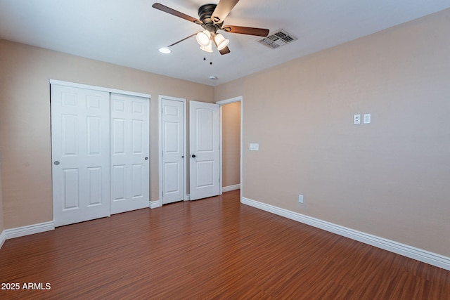 unfurnished bedroom featuring baseboards, visible vents, dark wood finished floors, and multiple closets