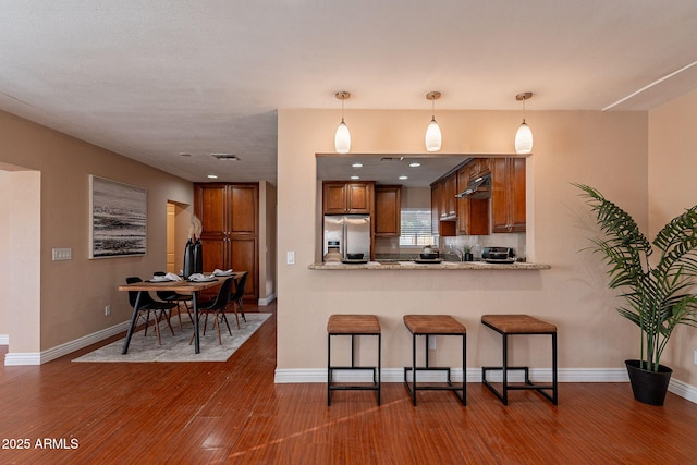 kitchen with a peninsula, a breakfast bar area, stainless steel refrigerator with ice dispenser, and dark wood-style flooring