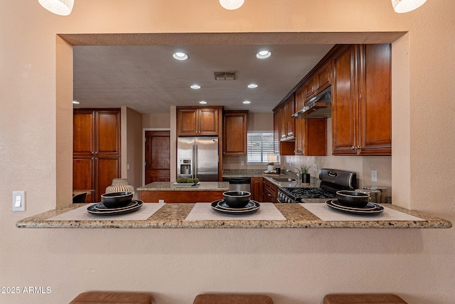 kitchen with visible vents, appliances with stainless steel finishes, brown cabinets, a peninsula, and under cabinet range hood