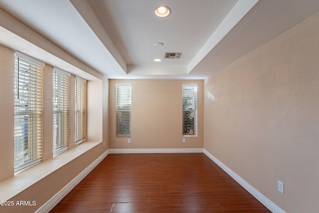 spare room featuring wood finished floors, a raised ceiling, visible vents, and baseboards