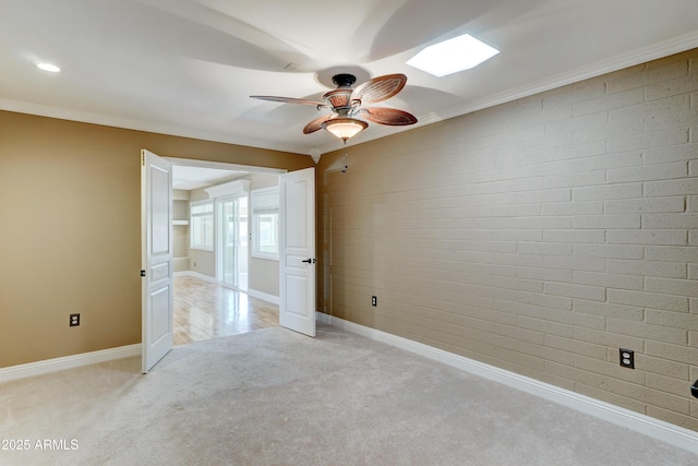 spare room featuring light carpet, ceiling fan, brick wall, and ornamental molding