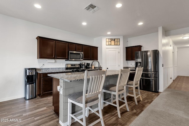 4595 W Foldwing Dr, San Tan Valley, AZ 85144 - kitchen featuring appliances with stainless steel finishes, wood finished floors, dark brown cabinets, a kitchen bar, and recessed lighting
