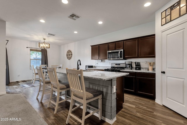 4595 W Foldwing Dr, San Tan Valley, AZ 85144 - kitchen with appliances with stainless steel finishes, a chandelier, a kitchen breakfast bar, dark brown cabinets, and a kitchen island with sink