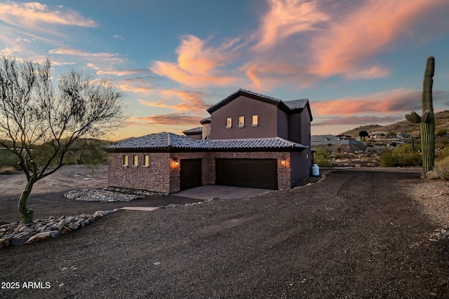 view of front of house with driveway, stone siding, a garage, and a tiled roof