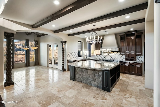 kitchen featuring arched walkways, a kitchen island, custom exhaust hood, backsplash, and light stone countertops