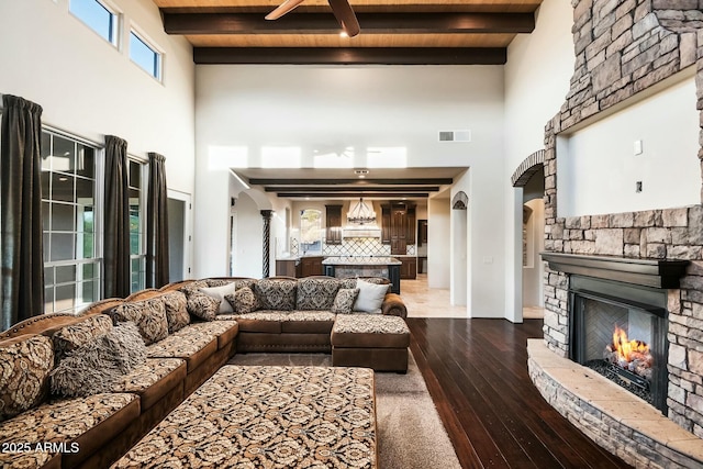 living area with arched walkways, dark wood finished floors, visible vents, a stone fireplace, and beamed ceiling