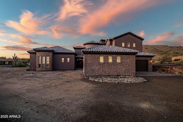 rear view of property with an attached garage, stone siding, a tile roof, and concrete driveway