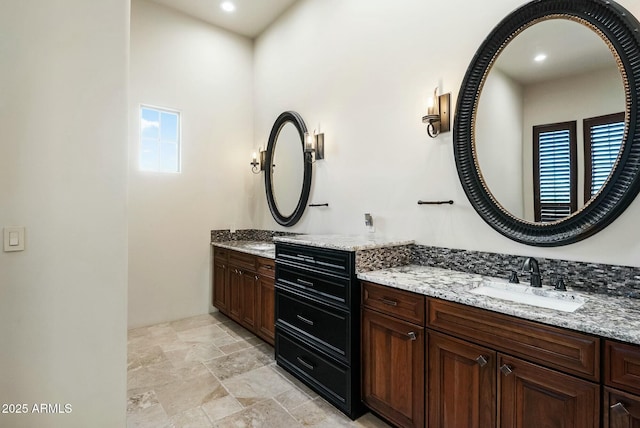 bathroom featuring recessed lighting, stone finish flooring, two vanities, and a sink