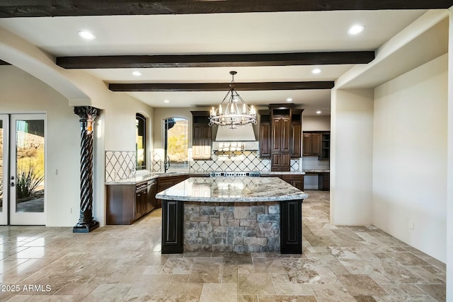 kitchen featuring light stone counters, backsplash, an inviting chandelier, a kitchen island, and dark brown cabinetry