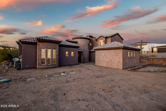 rear view of property featuring stone siding, a tile roof, and stucco siding