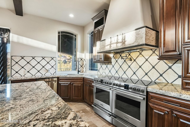 kitchen with custom range hood, backsplash, a sink, light stone countertops, and double oven range