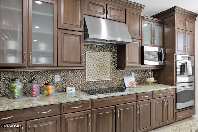 kitchen featuring decorative backsplash, light stone countertops, dark brown cabinets, and appliances with stainless steel finishes