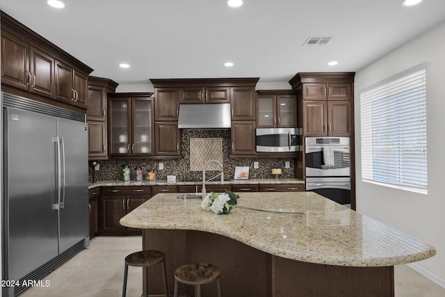 kitchen featuring dark brown cabinetry, stainless steel appliances, a breakfast bar area, and backsplash