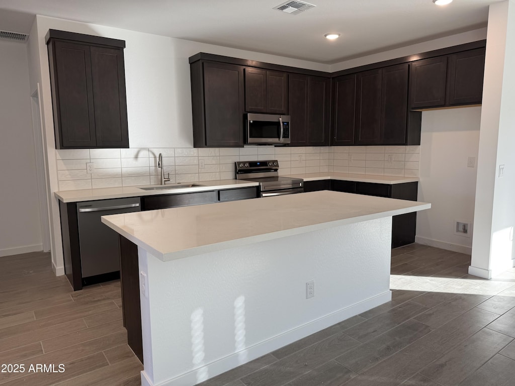 kitchen with dark brown cabinetry, a kitchen island, sink, backsplash, and appliances with stainless steel finishes