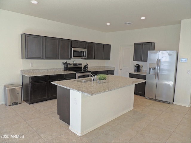 kitchen with sink, light stone counters, light tile patterned floors, an island with sink, and stainless steel appliances