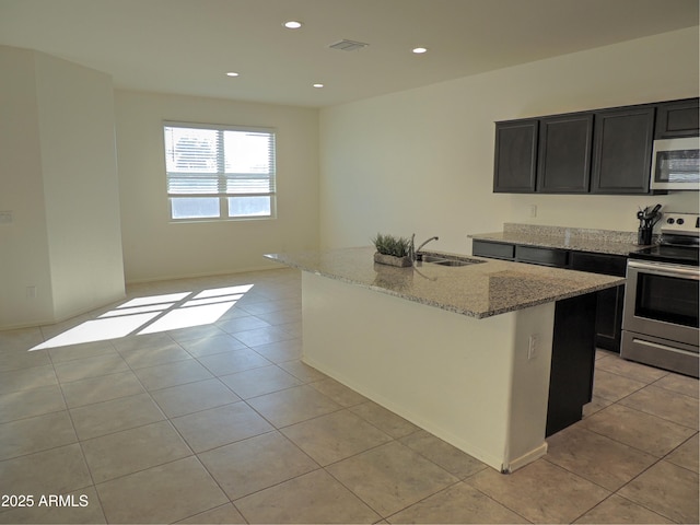 kitchen with sink, light stone counters, light tile patterned floors, appliances with stainless steel finishes, and a kitchen island with sink