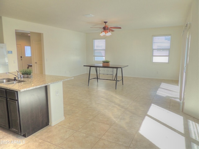 kitchen featuring sink, ceiling fan, light stone counters, dark brown cabinetry, and light tile patterned flooring