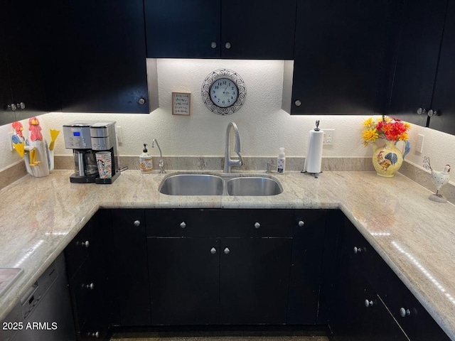 kitchen featuring dark cabinetry, a textured wall, and a sink