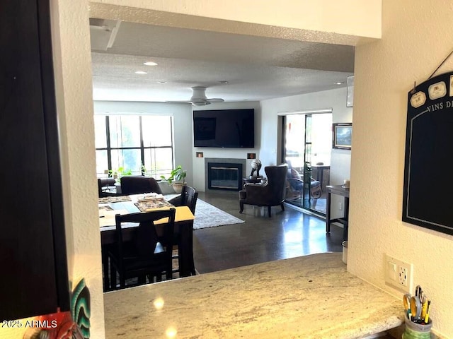 dining room featuring wood finished floors, a ceiling fan, a textured ceiling, a glass covered fireplace, and a textured wall