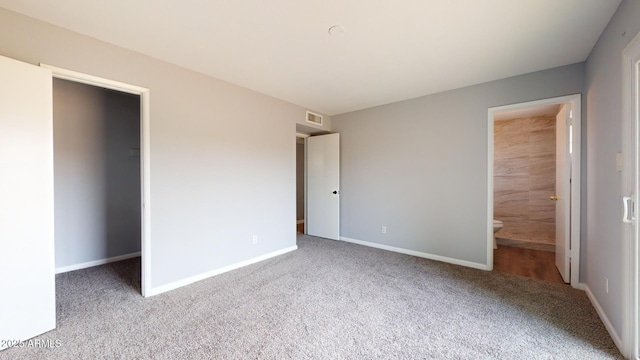 unfurnished bedroom featuring a walk in closet, ensuite bath, and carpet floors