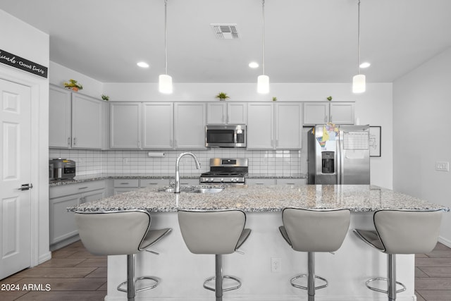 kitchen with a sink, stainless steel appliances, wood finish floors, and backsplash