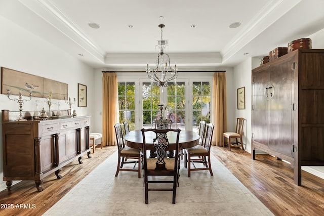 dining area with light wood-type flooring, an inviting chandelier, ornamental molding, and a raised ceiling