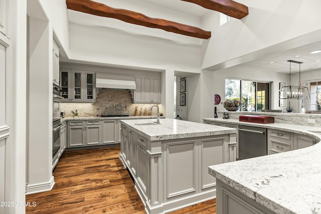 kitchen with an island with sink, appliances with stainless steel finishes, range hood, gray cabinets, and a sink