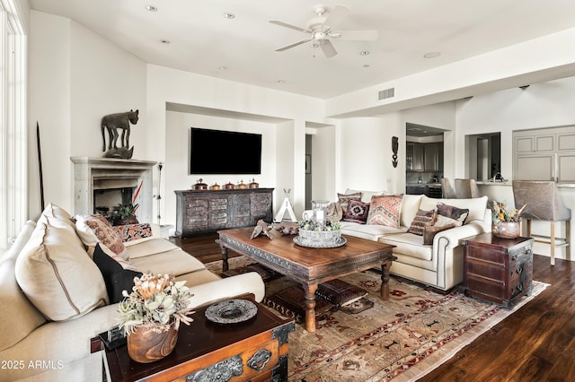 living room featuring dark wood-style floors, a fireplace, visible vents, and a ceiling fan