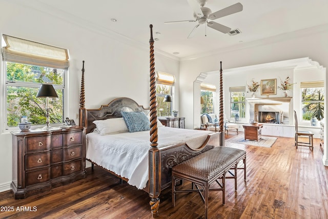 bedroom with a warm lit fireplace, multiple windows, visible vents, and crown molding