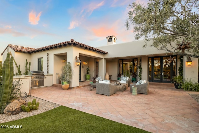 back of property at dusk featuring french doors, a patio area, an outdoor living space, and an outdoor kitchen